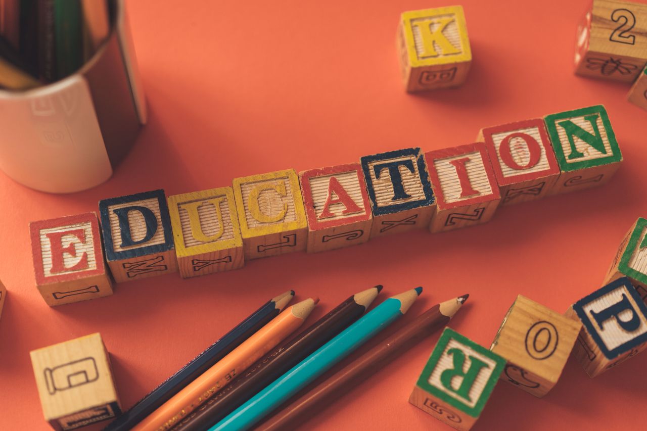 who-we-are Alphabet blocks spelling 'EDUCATION' on orange background with pencils.