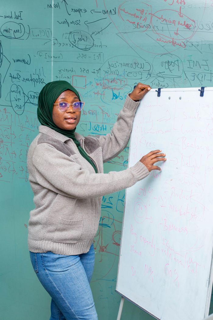 Crafting Captivating Headlines: Your awesome post title goes here Woman in hijab teaching with whiteboard in Lagos classroom, promoting education.