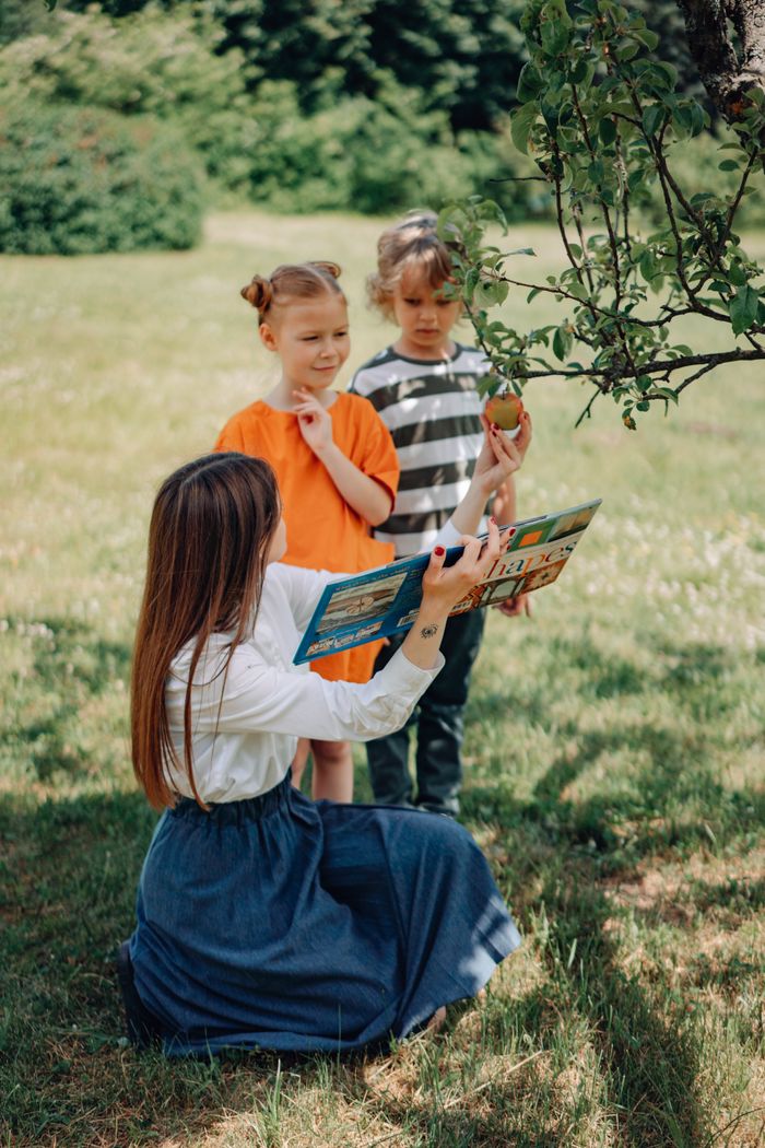 our-story A teacher reads to children under a tree, promoting outdoor education.